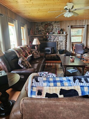 A cozy living room with a stone fireplace, leather sofa, and a wooden ceiling fan.