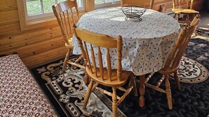 A cozy room with a wooden interior, a round table with chairs, and large windows offering a view of the outdoors.