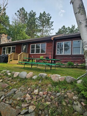 Una cabaña de troncos con un porche, una mesa de picnic y una chimenea de piedra.