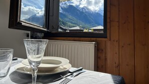 A table with a glass, plates, and cutlery set against a wooden wall with a window overlooking a mountain landscape.