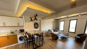 A modern apartment with a kitchen, dining area, and living room. It features wooden flooring, a dining table with chairs, a sofa, and a coffee table. - Oikos Bozcaada (Bozcaada)