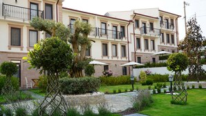 A multi-story hotel with balconies, a well-maintained garden with stone pathways, and outdoor seating areas. - Oikos Bozcaada (Bozcaada)