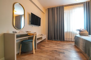 A modern bedroom with a wooden floor, a desk with a mirror, a television, and a bed with a view of the outdoors. - Oikos Bozcaada (Bozcaada)
