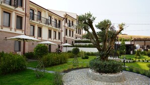 A courtyard with a central tree, surrounded by a stone pathway, and a building with balconies and outdoor seating. - Oikos Bozcaada (Bozcaada)