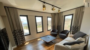A modern living room with a sofa, two armchairs, a coffee table, and large windows offering a view of the landscape. - Oikos Bozcaada (Bozcaada)
