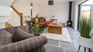 A modern living room with a brown leather sofa, a wooden coffee table, and a stone floor. There is a fireplace and a large window providing natural light. - Little Lugg (Hereford)