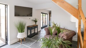 A modern living room with a staircase, a flat-screen TV mounted on the wall, a dark console table, and a potted plant. - Little Lugg (Hereford)