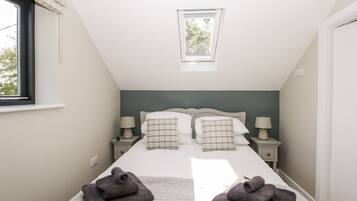 Una camera da letto con un letto grande, due comodini con lampade, una finestra con persiane e un velux.