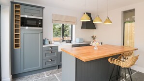 A modern kitchen with grey cabinets, a wooden island, and a window with a view of greenery. - Little Lugg (Hereford)