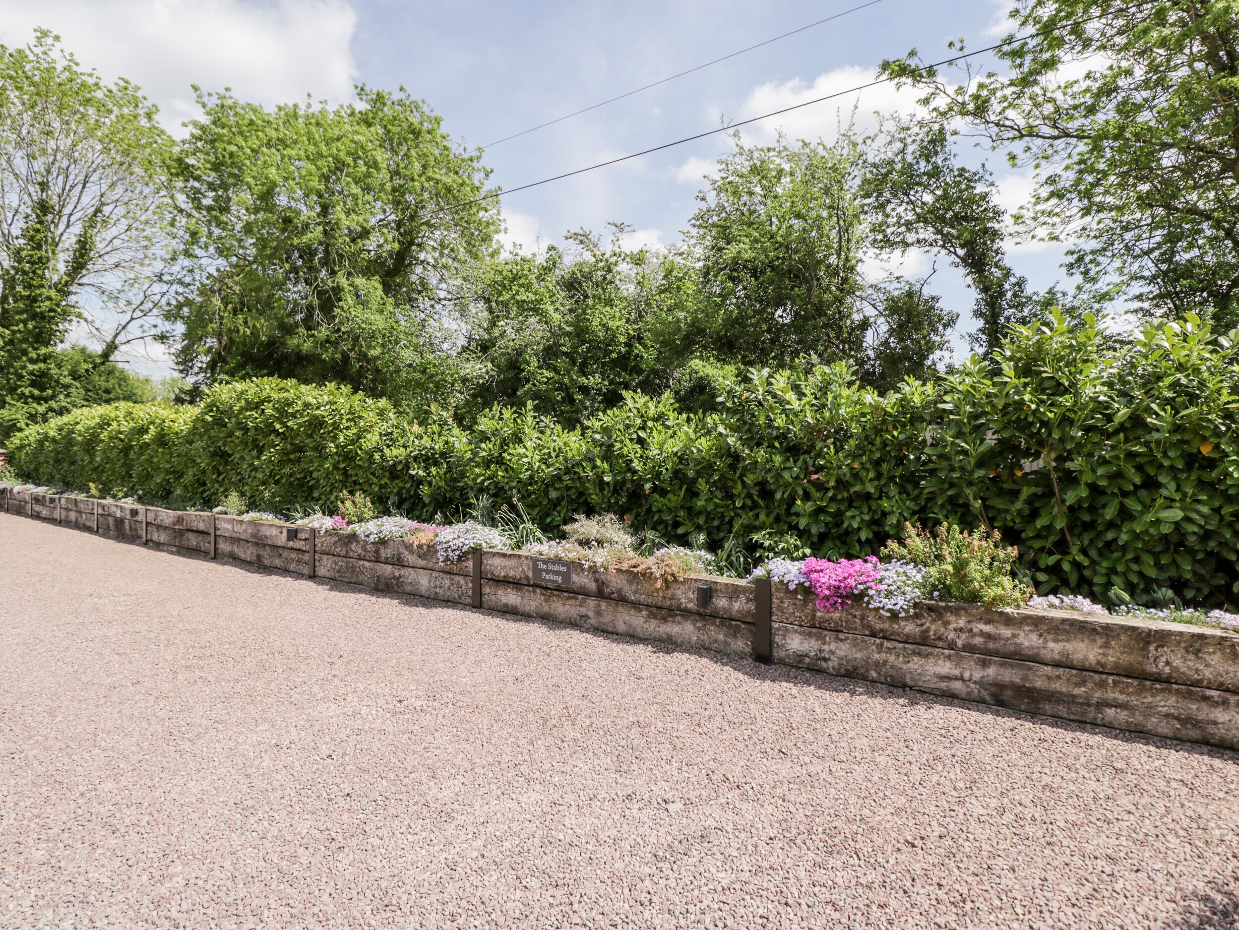 A gravel parking area with a stone wall and a sign indicating 'The Stables Parking'.