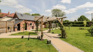 A rustic building with a wooden pergola, a brick exterior, and a paved pathway leading to a grassy area. - Little Lugg (Hereford)