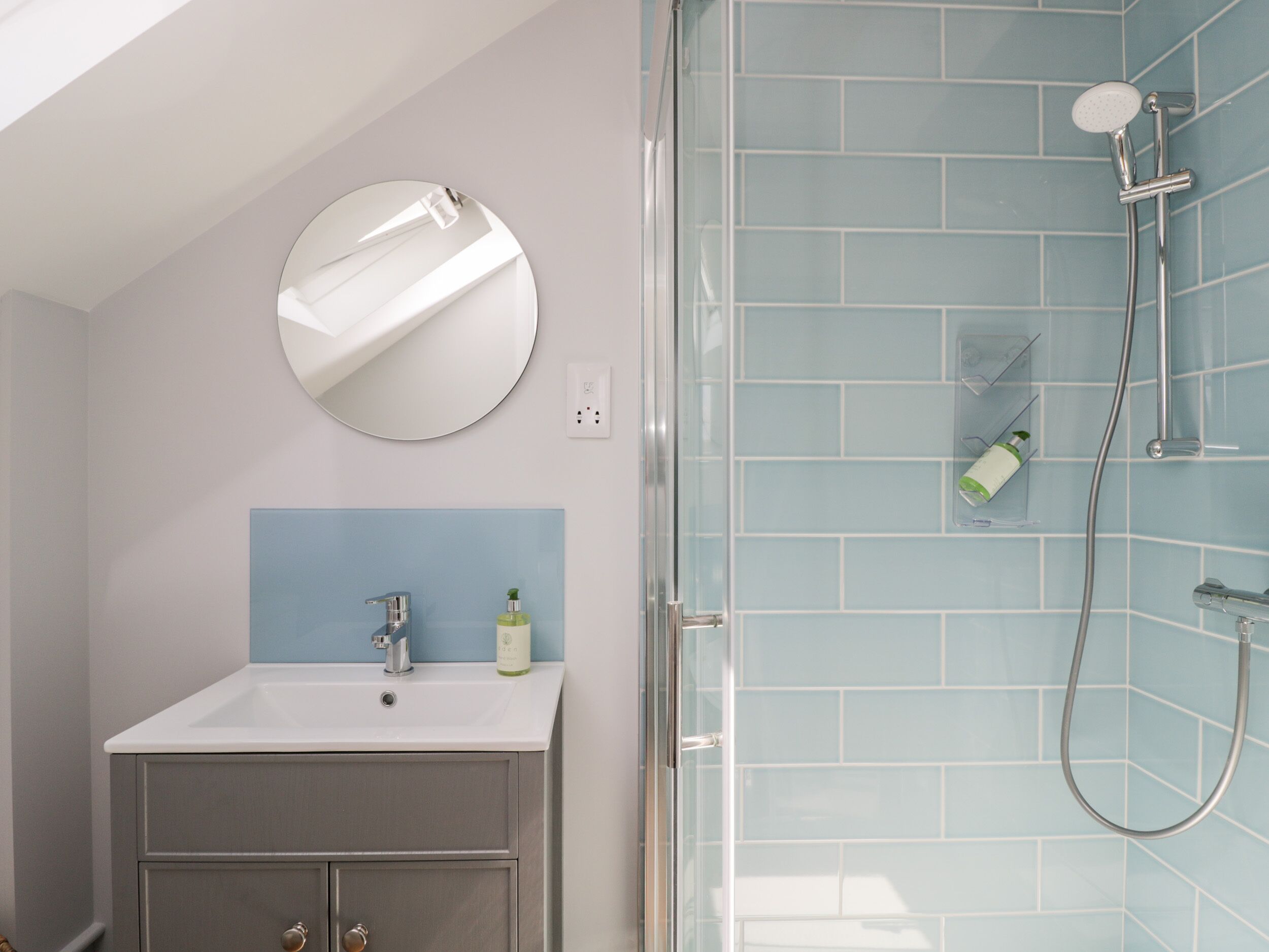 A bathroom with a white sink, a mirror, and a shower with blue tiles.