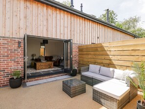 An open patio area with a brick wall, wooden deck, and outdoor furniture including a sofa and a coffee table. - Little Lugg (Hereford)