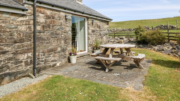 A stone cottage with a tiled patio, a wooden table, and a potted plant. - Orsedd Wen Cottage (Llanrwst)