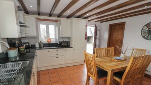 A kitchen with white cabinets, a black countertop, and a wooden dining table with chairs. - Orsedd Wen Cottage (Llanrwst)