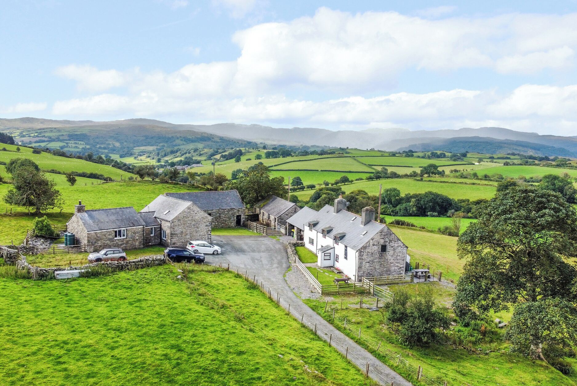 A rural setting with stone buildings, a gravel driveway, and green fields.