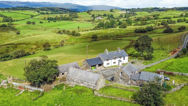 Une maison en pierre à la façade blanche, entourée de champs verdoyants et d’un paysage rural.