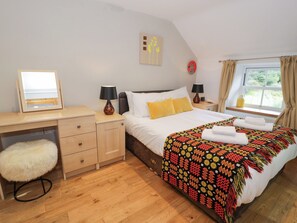 A bedroom with a bed, two bedside tables, a desk, a chair, a window with curtains, and a wall decoration.