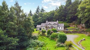 A stone house with a traditional design, surrounded by lush greenery and a stone wall.