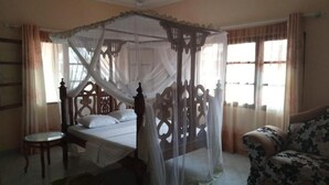 Un dormitorio con cama con dosel, ventilador de techo, una pequeña mesa redonda y un sofá.