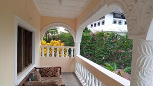Un balcón con banco de madera, baranda blanca y vistas a un jardín con plantas en flor.