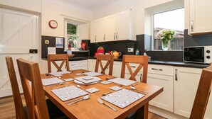 A modern kitchen with white cabinets, a dining table set for four, and a window with a view of greenery outside. - North Lodge (Forfar)