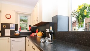 A modern kitchen with a dishwasher, a yellow teapot, wine glasses, and a bottle of wine on the counter. - North Lodge (Forfar)