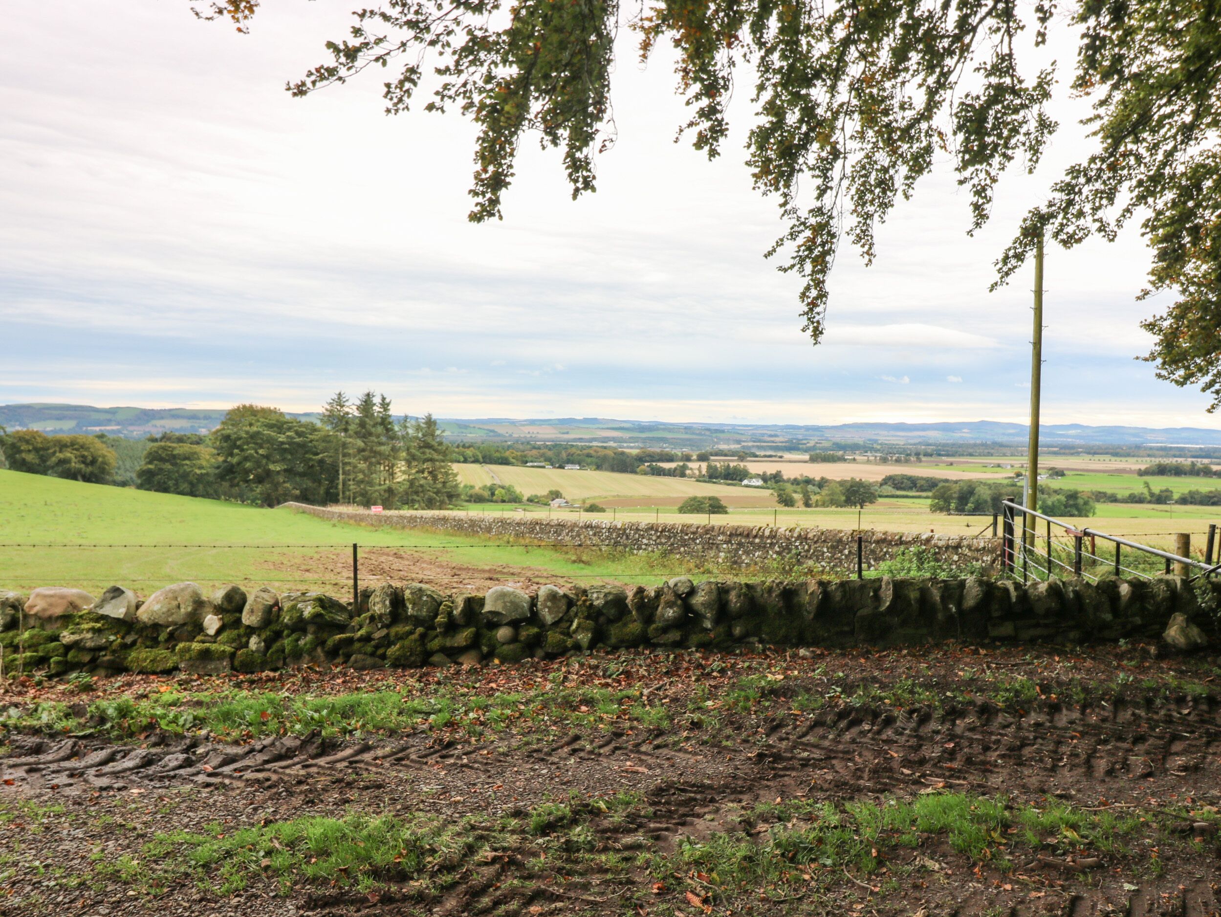 A rural landscape with a stone wall, grassy fields, and distant hills.