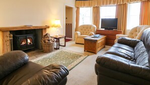 A living room with a fireplace, leather sofas, a television, and a large window with curtains. - North Lodge (Forfar)