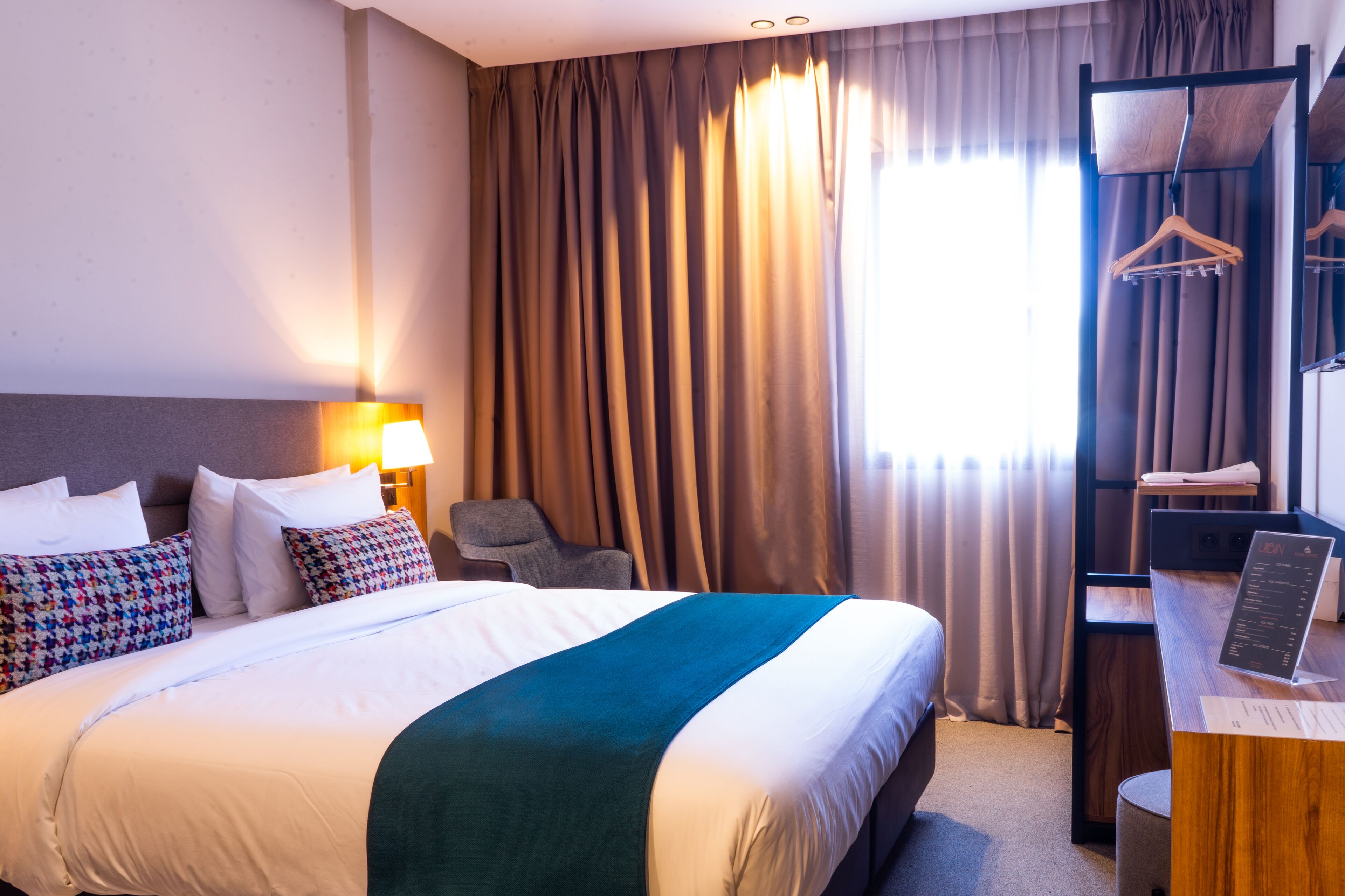 Habitació d'hotel amb un llit gran, una taula de treball amb un ordinador portàtil, una cadira i un armari amb penjadors.