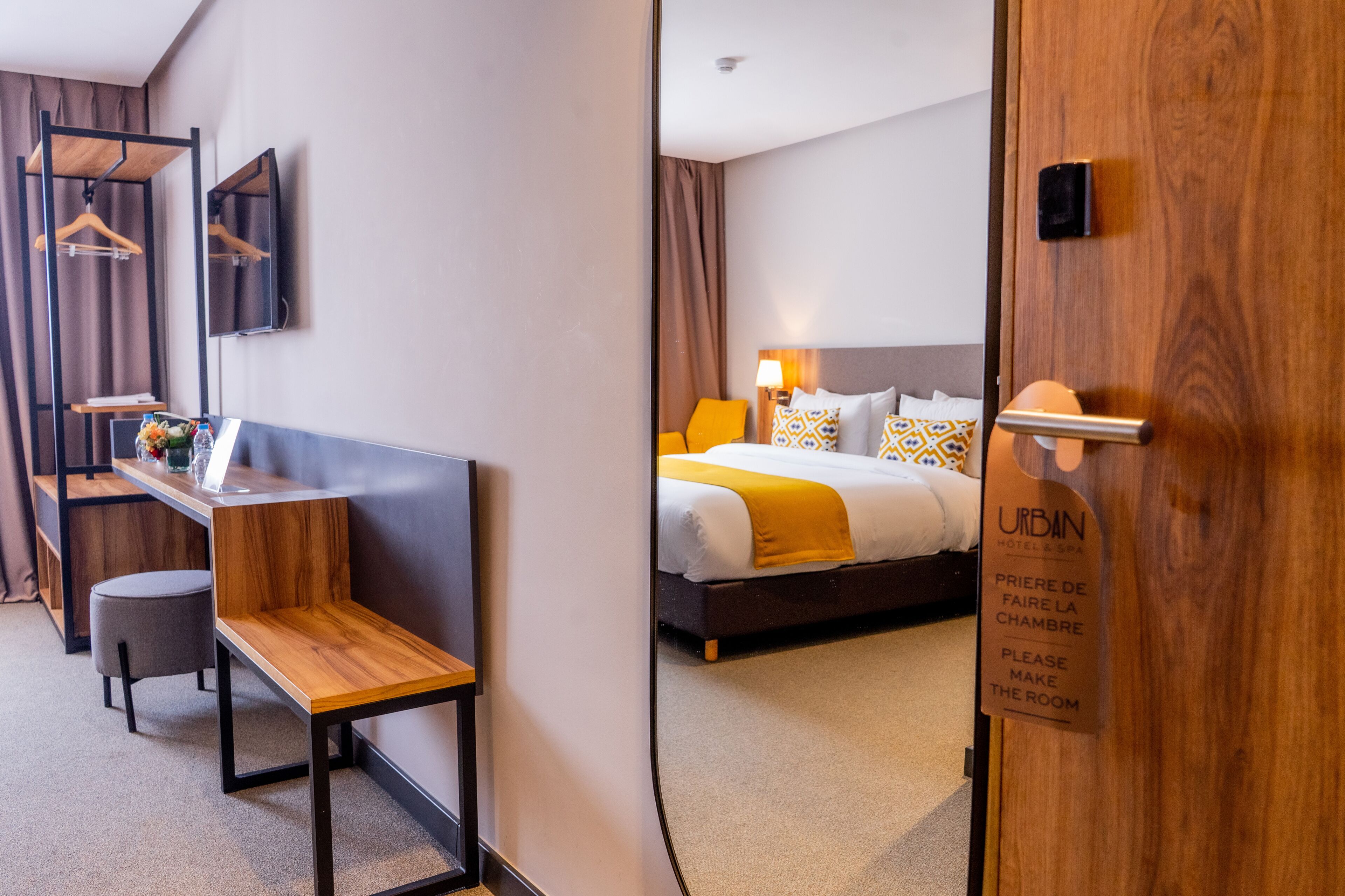 A hotel room with a bed, bedside table, chair, and a mirror.