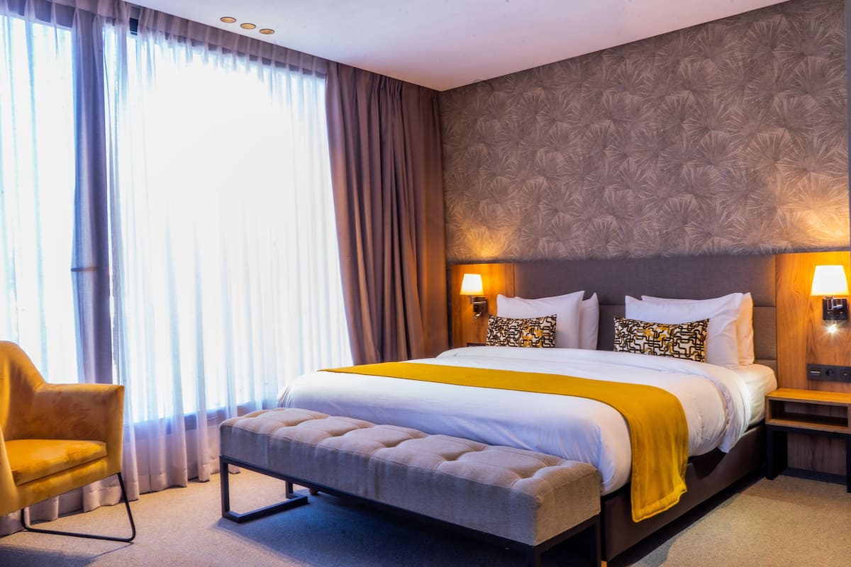 A hotel room with a large bed, a bedside table, a chair, and a window with curtains.