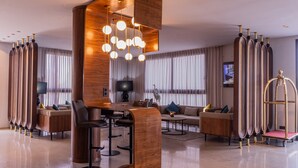 A modern hotel lobby with a wooden reception desk, bar seating, sofas, and a large chandelier. - Urban Hotel and Spa (Kenitra)