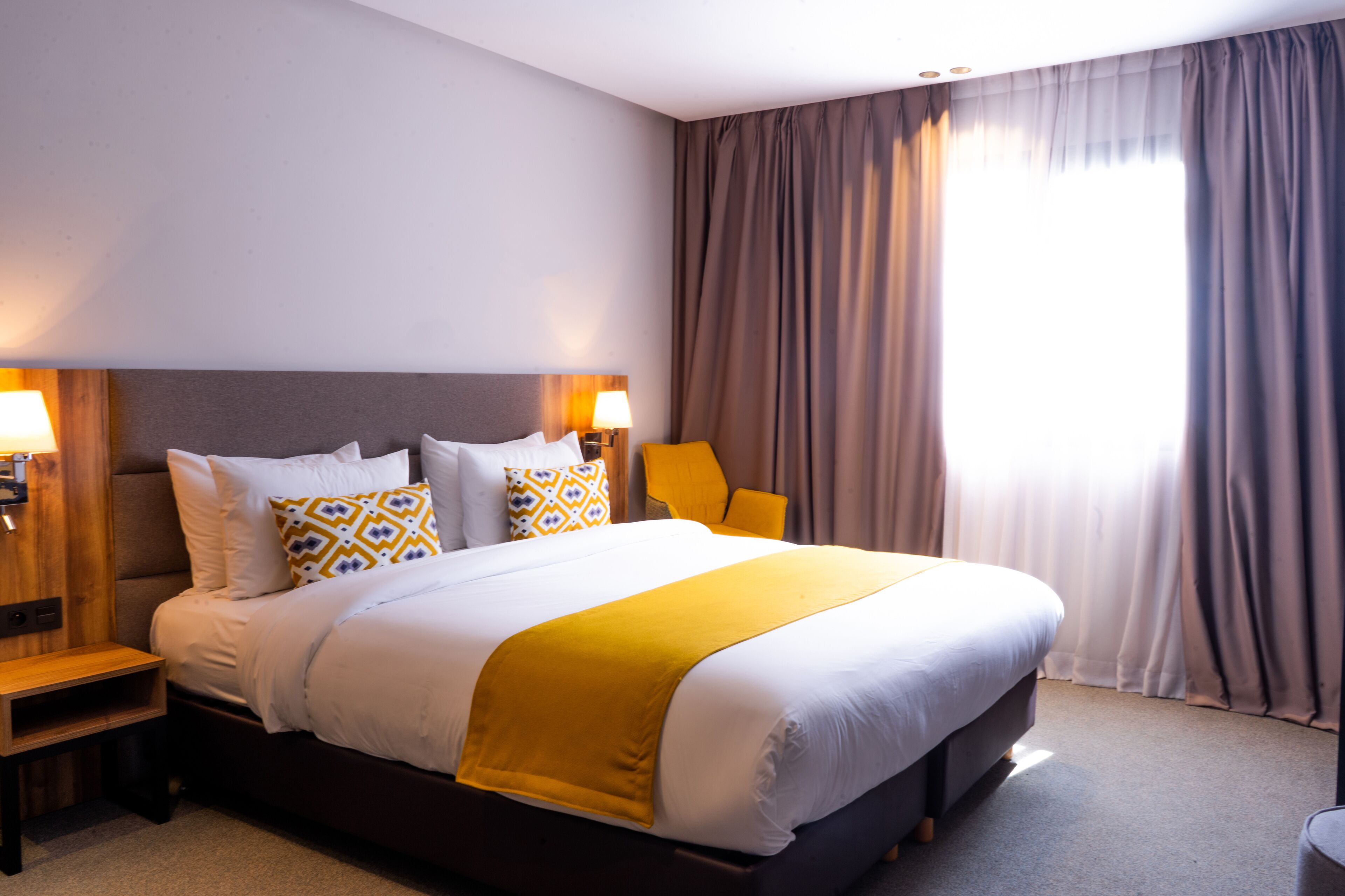 A hotel room with a large bed, two bedside tables, a nightstand, and a window with curtains.