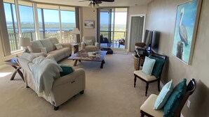 Un salon spacieux avec un grand canapé, une table basse et un téléviseur. Il y a un balcon avec vue sur l’océan.