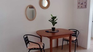 A dining area with a wooden table, two black chairs with cushioned seats, a small potted plant, and three wall-mounted mirrors.