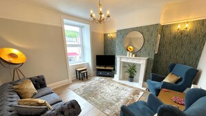A living room with a grey sofa, a blue armchair, a flat-screen TV, a fireplace, and a large window.