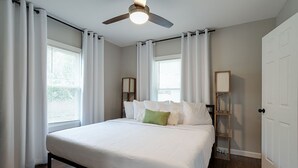 Une chambre à coucher avec un lit, des rideaux blancs, un ventilateur de plafond et une table de chevet avec une lampe.