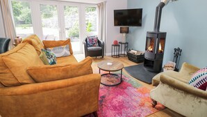 A living room with a sofa, armchair, TV, fireplace, and a view through large windows. - Pengwern Bach (Llanrwst)