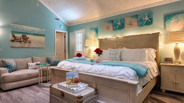 Un dormitorio con cama, mesita de noche, cómoda, silla, mesa y obras de arte en las paredes.
