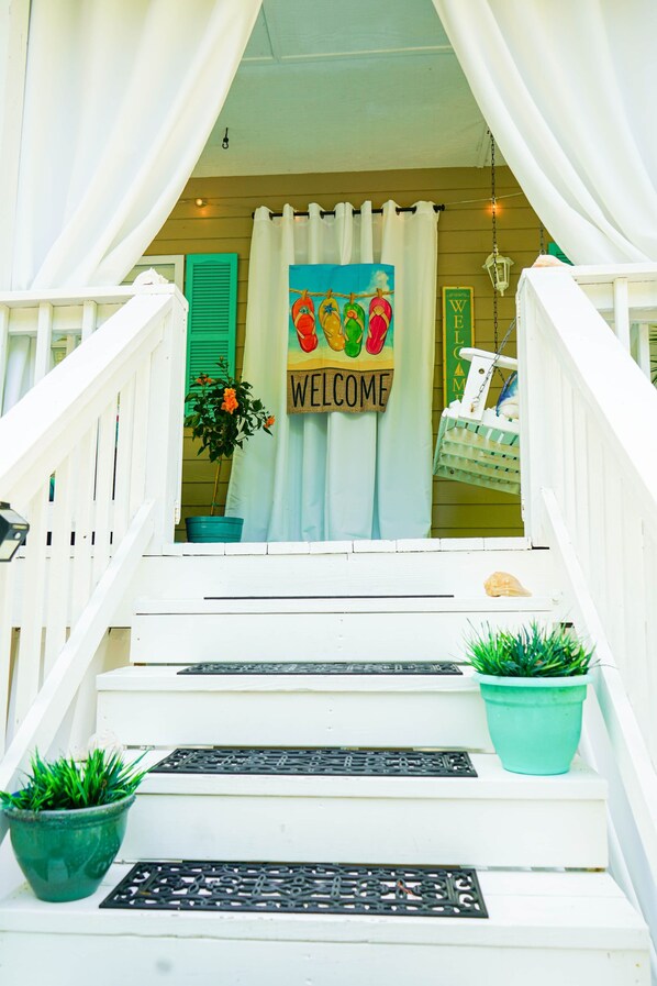 Una escalera con un letrero de 'WELCOME', plantas en macetas y un farol colgante.