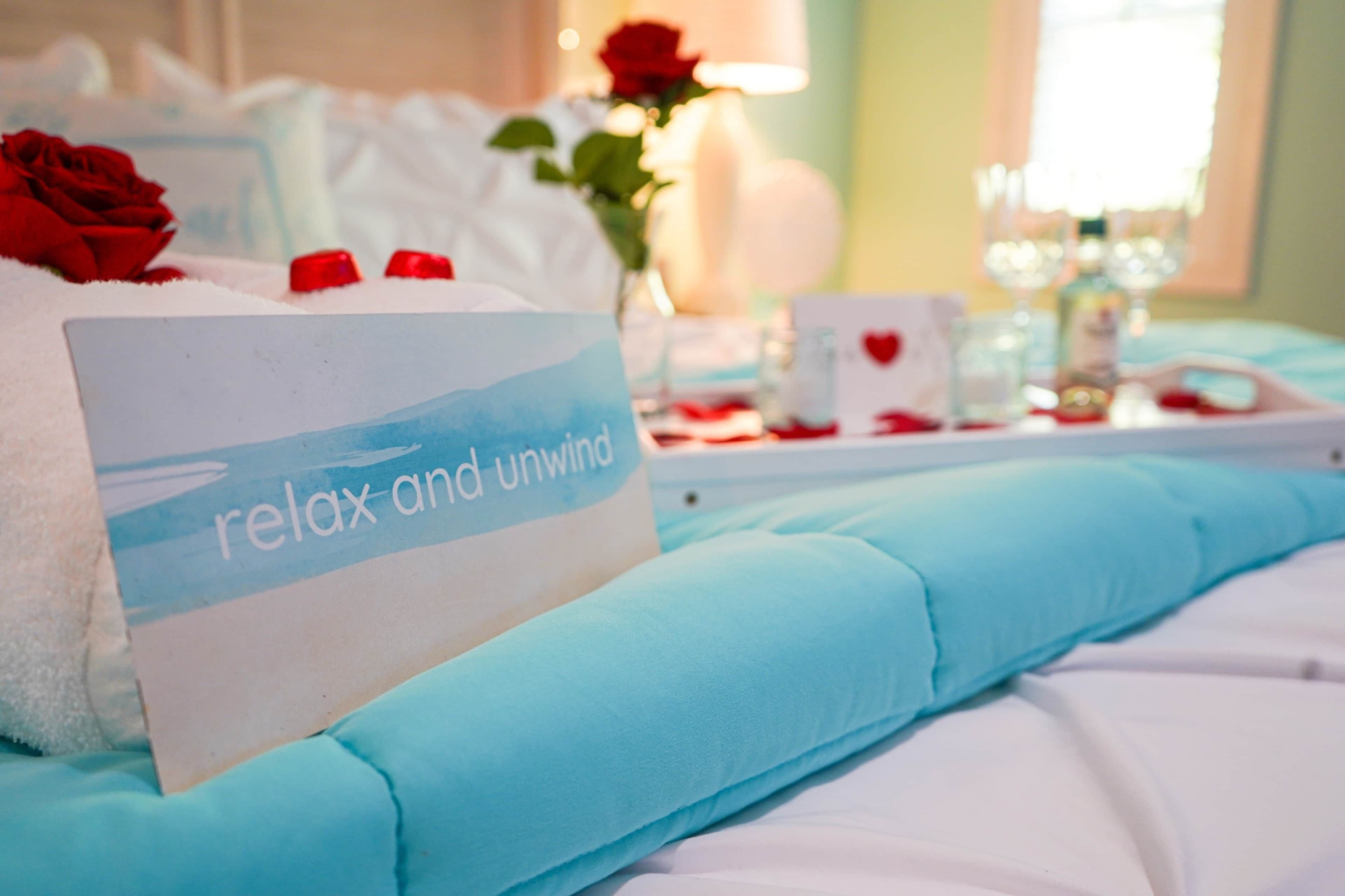 A bed with a sign reading 'relax and unwind,' a rose, and a tray with rose petals.