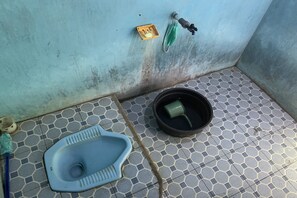Een kleine betegelde badkamer met een blauw toilet, een groen gezichtsmasker dat aan de muur hangt, en een geel zeepbakje.