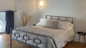 Un dormitorio con estructura de cama metálica, mesita de noche con un objeto esférico y lámpara de pared.