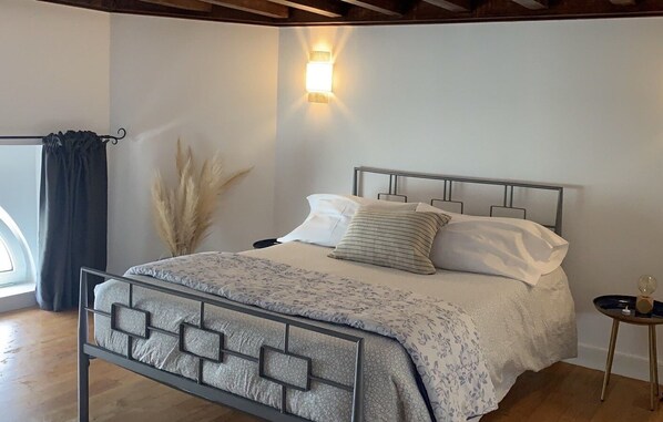 A bedroom with a metal bed frame, a bedside table with a spherical object, and a wall-mounted light fixture.