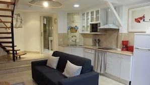 Una cocina moderna con armarios blancos, un sofá negro con almohadones a rayas, una escalera de madera y una cafetera roja.