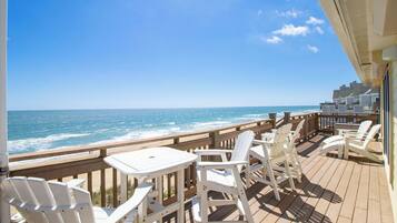 A wooden deck with white chairs and tables overlooking the ocean.