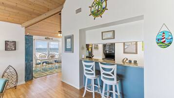 A kitchen area with a bar, white bar stools, and a sign indicating beach rules.