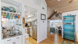 A spacious kitchen with a wooden ceiling, white cabinetry, and a variety of colorful kitchenware on shelves. - Luxury, Ocean Front, Cargo Lift, 3rd Floor Penthouse KD0003 (Kill Devil Hills)