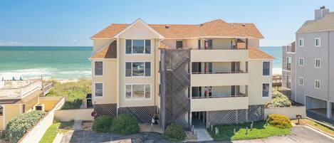 A multi-story building with a balcony, located near a beach with a clear view of the ocean.